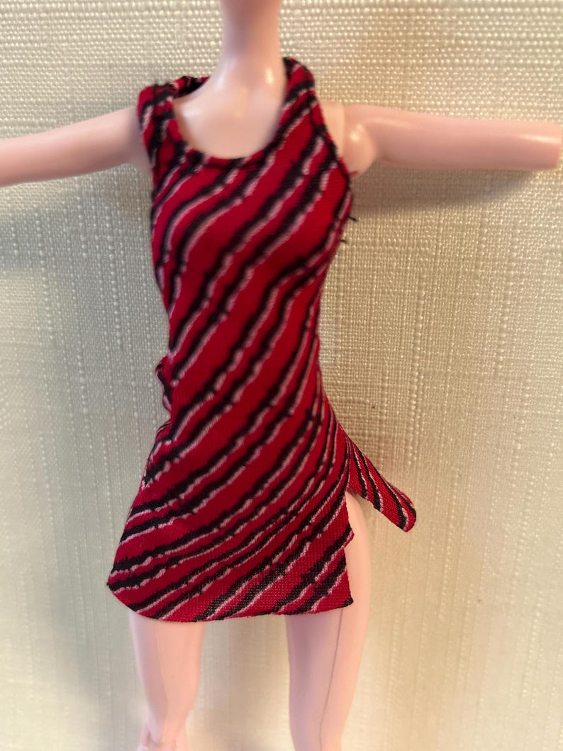 Puede incluir: Vestido de mu&ntilde;eca a rayas rojas y negras, con cuello halter y abertura lateral. El vestido sin mangas es de tejido. Las rayas diagonales crean un patr&oacute;n din&aacute;mico. Vestido para mu&ntilde;eca.