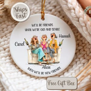 May include: A white ceramic ornament with a gold string, featuring a watercolor illustration of three women laughing and holding bottles. Text reads "We'll be friends until we're old and senile." Names "Carol," "Alicia," and "Hannah" are included.