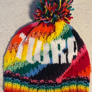 May include: A rainbow knit beanie with a white pom pom and the word "WARP" knitted in white on the front.