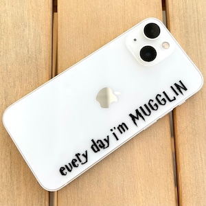 May include: White iPhone case with a black sticker that says "every day i'm mugglin".