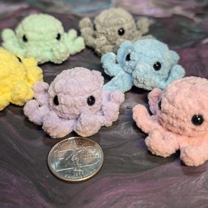 May include: A collection of six crocheted octopus plushies in various pastel colors, including yellow, light green, lavender, light blue, and pink. Each octopus has black eyes and eight tentacles.