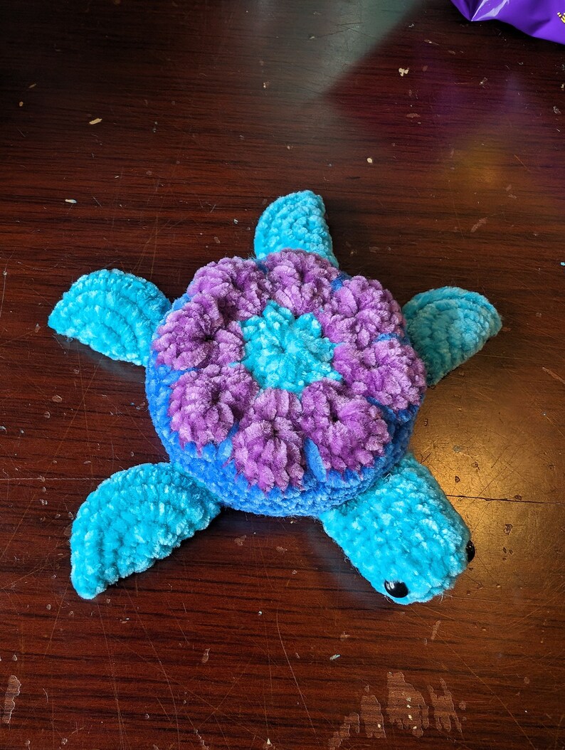 May include: A crocheted stuffed sea turtle toy with a blue and purple shell. The shell has a flower design in the center.