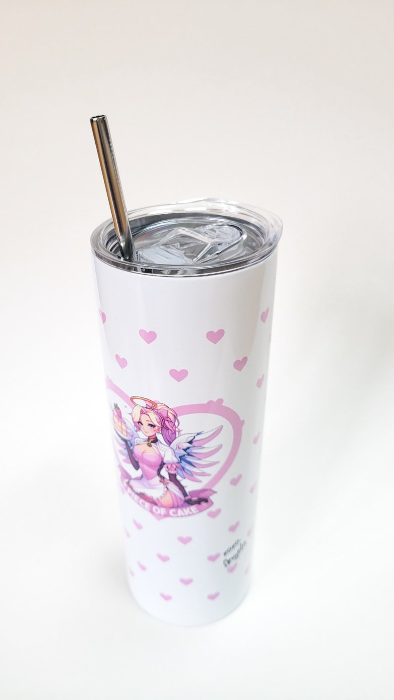 Puede incluir: Un vaso de acero inoxidable blanco con un patr&oacute;n de corazones rosas y una ilustraci&oacute;n rosa y blanca de un personaje femenino con alas y un halo. El vaso tiene una tapa transparente y una pajita de acero inoxidable. El texto "A Piece of Cake" y "xoxo Angela" est&aacute;n impresos en el vaso.