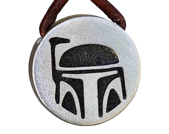 May include: A silver pendant necklace with a brown leather cord. The pendant features a black and white silhouette of a Star Wars Boba Fett helmet.