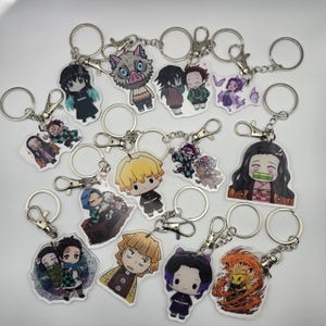 May include: A selection of anime character keyrings. Each keyring has a silver-coloured ring and clasp. The character designs are colourful and detailed, with a variety of poses and expressions. The keyrings are made of a clear, glossy material.