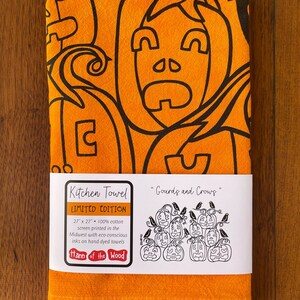May include: Orange kitchen towel with a black graphic design of pumpkins and crows. The towel is 27 x 27 inches and made of 100% cotton. The towel is a limited edition and is screen printed with eco-conscious inks.