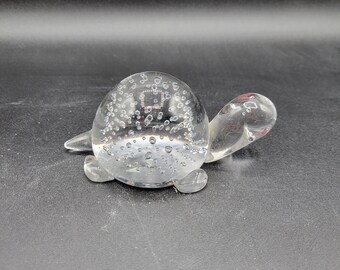 May include: A clear glass turtle figurine with a bubble-filled shell. The turtle is sitting on a black surface.
