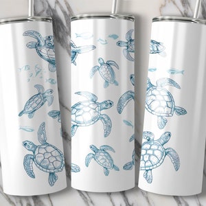 May include: White insulated tumbler featuring a blue sea turtle and fish pattern. The design includes multiple sea turtles of varying sizes, with fish swimming around them. The tumbler has a silver lid and a straw.