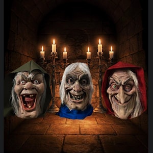 May include: Three grotesque Halloween masks with exaggerated features and aged skin. The masks are lit by candlelight, creating a spooky atmosphere. One mask wears a green hood, another a blue scarf, and the third a red hood.