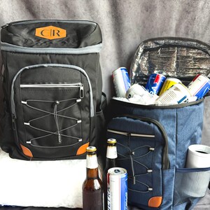 May include: Two insulated cooler backpacks, one black and one blue, with multiple pockets and a bungee cord design. The black backpack has a brown leather patch with the letters "CR". The blue backpack is open, filled with ice and cans of beer. Beer bottles and cans are in front.