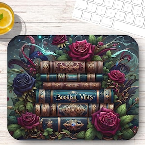 May include: A decorative mousepad featuring a stack of books with gold accents and the words "Bookish Vibes". The books are surrounded by burgundy and blue roses and green foliage. A keyboard and mouse are in the background.