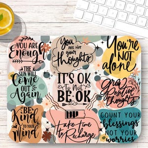 May include: A rectangular mousepad with a colorful design featuring inspirational quotes in black script on pastel-colored shapes. Quotes include "You are enough," "You are not your thoughts," and "You're not alone."