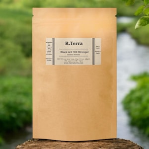 May include: A brown paper bag with a label that reads "R.Terra Black Ant 10X Stronger Extract Powder" and a website address. The bag is sitting on a wooden surface in front of a green and brown background.