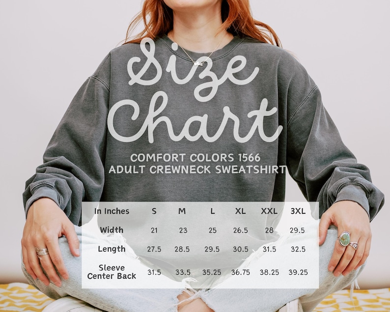 Op de afbeelding: Een grijze Comfort Colors 1566 sweatshirt voor volwassenen met een maattabel. De tabel toont de afmetingen in centimeters voor breedte, lengte en mouwrug voor de maten S t/m 3XL.