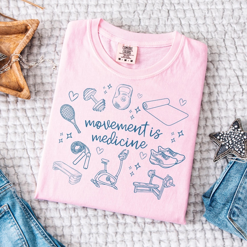 May include: Pink t-shirt with a blue graphic of fitness equipment and the text "movement is medicine".