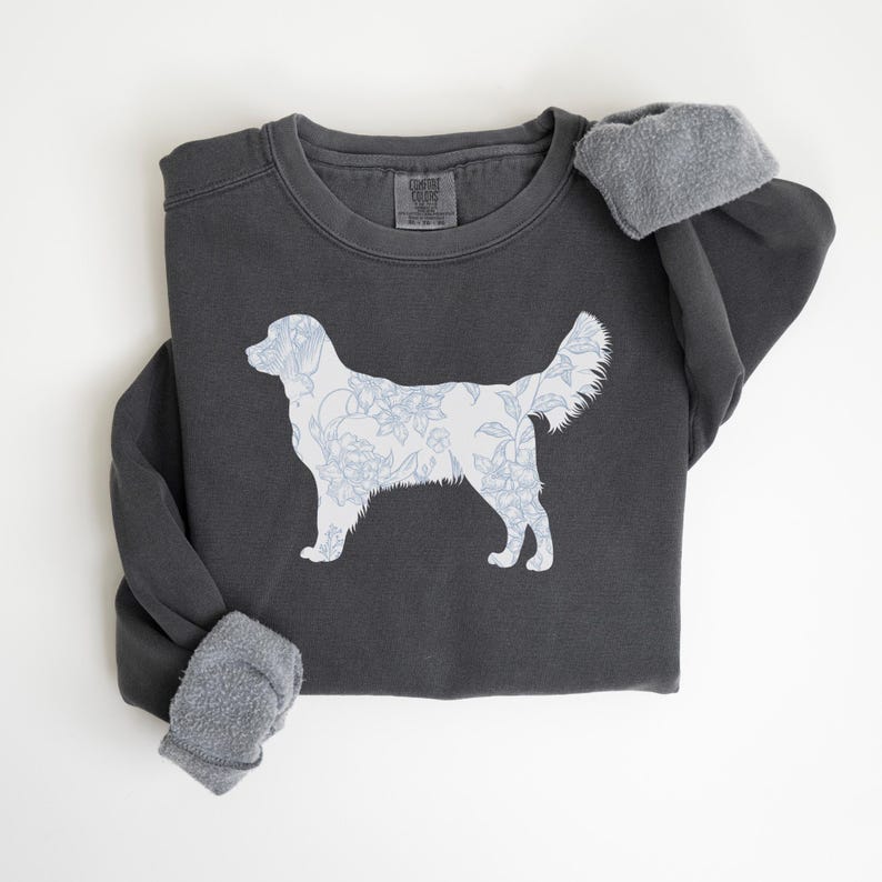 Op de afbeelding: Donkergrijze sweatshirt met een wit honden silhouet gevuld met een blauw bloemenpatroon. De sweatshirt heeft een ronde hals en lange mouwen met grijze fleece manchetten. Het ontwerp is gecentreerd op de voorkant.