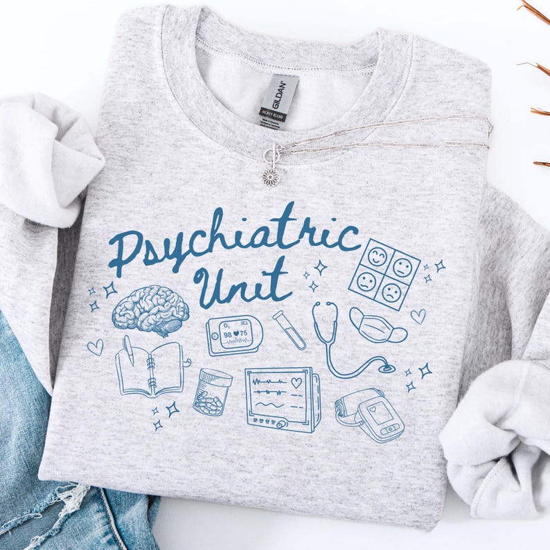May include: Gray sweatshirt with the text "Psychiatric Unit" in blue lettering. The sweatshirt features a variety of blue medical illustrations, including a brain, a stethoscope, a face mask, a pill bottle, a notebook, a heart rate monitor, and a blood pressure cuff.