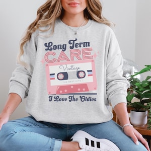 May include: A grey sweatshirt with a pink cassette tape graphic and the text "Long Term Care Vintage - The Best Hits - I Love The Oldies".
