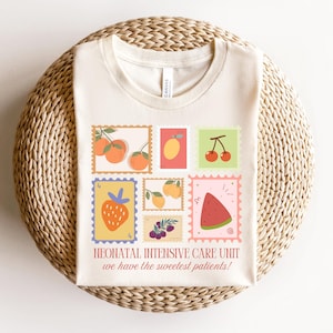 May include: A beige t-shirt with a graphic of colorful fruit stamps. The text "Neonatal Intensive Care Unit we have the sweetest patients!" is printed on the shirt.