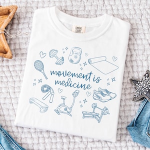 May include: White t-shirt with a blue graphic design of various fitness equipment and the text "movement is medicine".