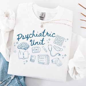 May include: White sweatshirt with blue text that reads "Psychiatric Unit" and blue illustrations of medical equipment, including a brain, a stethoscope, a notebook, a pill bottle, a blood pressure cuff, and a heart monitor.