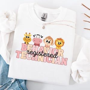 May include: White sweatshirt with a pink and white graphic design that says "Behavior registered technician" with a giraffe, cow, monkey, and lion illustration.