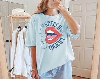 May include: A light blue t-shirt with a graphic of a red open mouth with the text "Speech Therapy" in blue.