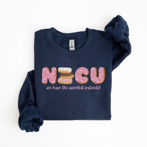 Pode incluir: Uma camisa de moletom azul marinho com um gr&aacute;fico de donuts que soletram "NICU" e o texto "we have the sweetest patients!"