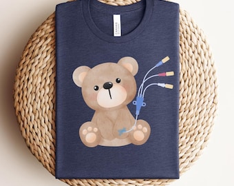 May include: A navy blue t-shirt with a brown teddy bear wearing a medical IV. The bear has a light brown nose and light brown paw pads.
