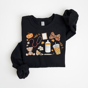 May include: Black sweatshirt with a fall-themed design featuring a pumpkin, stethoscope, teddy bear, baby bottle, coffee cup, and a bow.