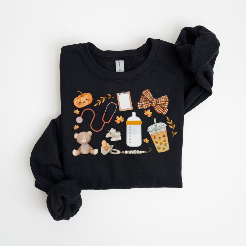 May include: Black sweatshirt with a fall-themed design featuring a pumpkin, stethoscope, teddy bear, baby bottle, coffee cup, and a bow.
