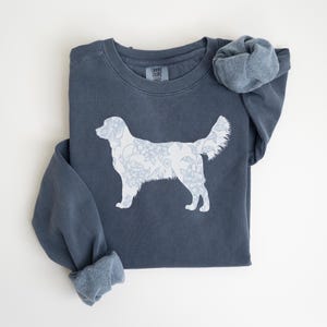 Op de afbeelding: Een marineblauw sweatshirt met een witte bloemenhondsilhouet. Het hondenontwerp is gevuld met een delicaat bloemenpatroon. De sweatshirt heeft een ronde hals en lange mouwen met manchetten. Het Comfort Colors-merkteken is zichtbaar.