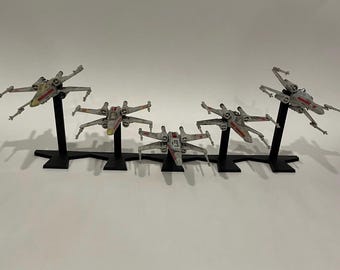 May include: Five Star Wars X-Wing fighter model spaceships on black stands. The spaceships are painted in a weathered gray and white color scheme with red accents.