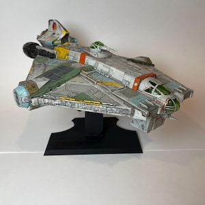 May include: A white, green, and yellow model of a spaceship with a black stand. The spaceship has a green cockpit and a green and yellow tail.