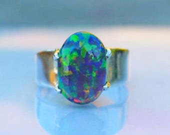 May include: A silver ring featuring an oval-cut opal gemstone. The opal displays a vibrant play-of-color with hues of blue, green, and purple. The ring's band is a simple, polished silver design, showcasing the gemstone's beauty.