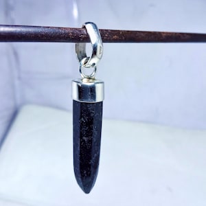 May include: A black gemstone pendant with a silver setting. The pendant is shaped like a point and is hanging from a silver bail.