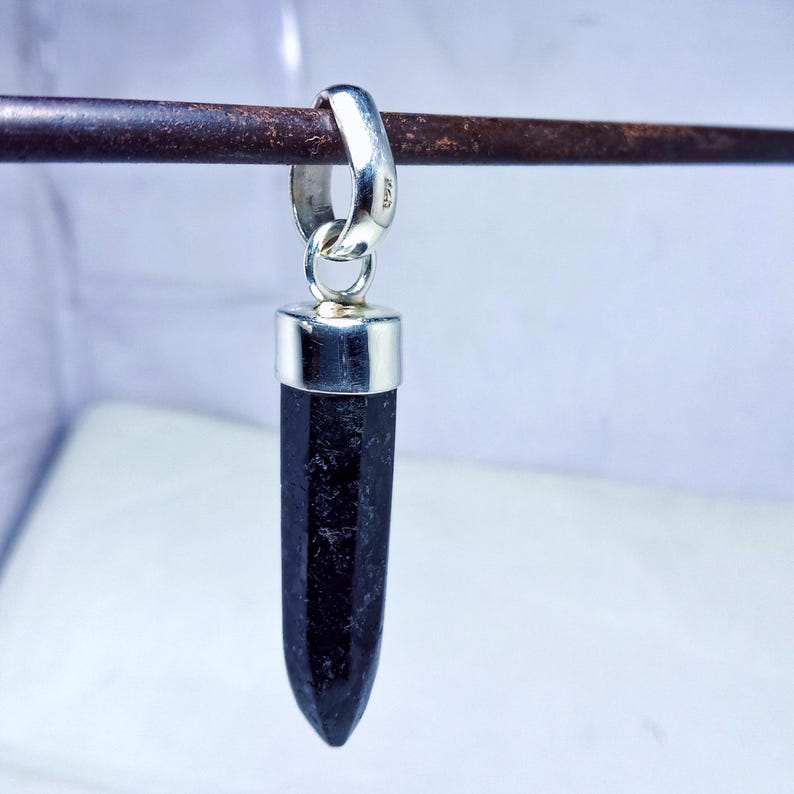 May include: A black gemstone pendant with a silver setting. The pendant is shaped like a point and is hanging from a silver bail.
