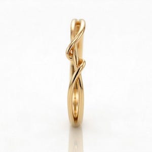 Op de afbeelding: Een goudkleurige ring met een uniek, verweven ontwerp. De ring heeft een continu, vloeiend patroon dat zich om de band wikkelt. Het ontwerp van de ring is elegant en modern, geschikt voor dagelijks gebruik of speciale gelegenheden.