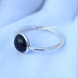 May include: A silver ring with a black gemstone. The ring is simple and elegant, and the gemstone is set in a bezel setting.