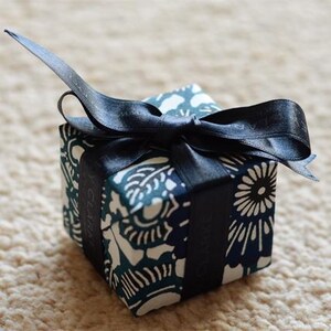 May include: A small, blue and white patterned gift box with a black ribbon tied in a bow. The box is tied with a black ribbon and has a white label with the word "GIVEN" printed on it.