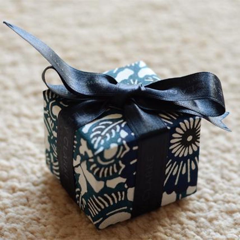 May include: A small, blue and white patterned gift box with a black ribbon tied in a bow. The box is tied with a black ribbon and has a white label with the word "GIVEN" printed on it.
