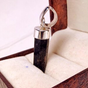 May include: A black gemstone pendant with a silver bail and setting. The pendant is in a small, white velvet box with a brown wooden exterior.