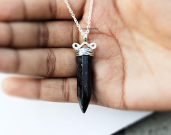 May include: A black gemstone pendant with a silver wire wrap and a silver chain. The pendant is shaped like a point and is about 2 inches long.