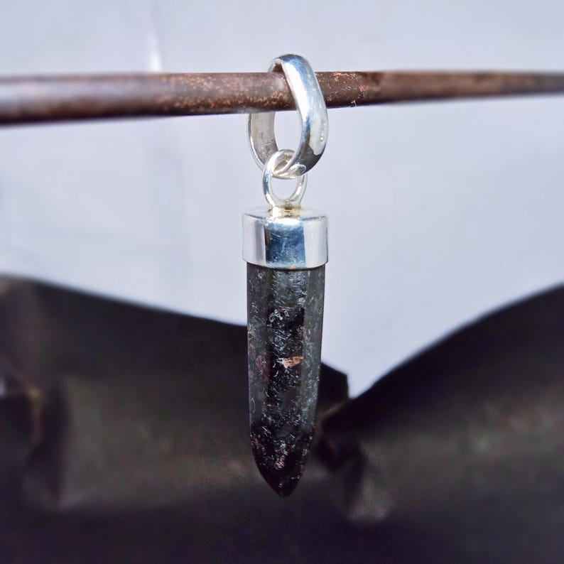 May include: A silver pendant with a black gemstone in the shape of a point. The pendant is hanging from a silver loop.