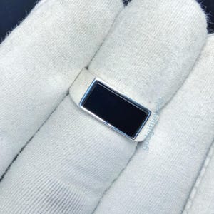 Könnte beinhalten: Ein silberner Ring mit einem schwarzen rechteckigen Stein in der Mitte.