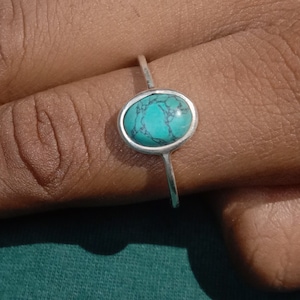 May include: A silver ring with a turquoise gemstone. The ring is on a person's finger.