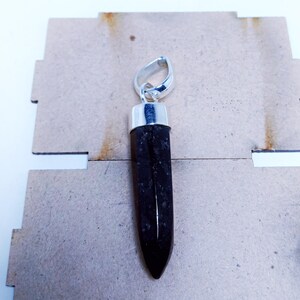 May include: A black gemstone pendant with a silver bail. The gemstone is a long, pointed shape and has a rough, textured surface.