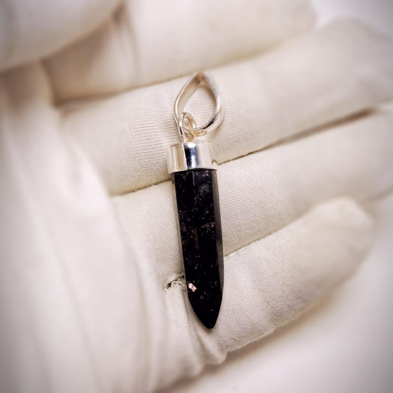 May include: A silver pendant with a black gemstone in the shape of a point. The pendant is on a white surface.