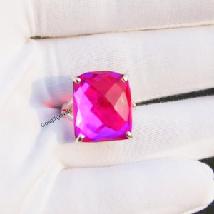May include: A silver ring with a large, faceted, pink gemstone. The gemstone is a cushion cut and has a slight purple hue.