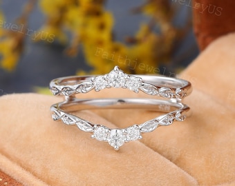 May include: A delicate silver ring set with small diamonds. The ring is designed with a curved, leaf-like pattern. The set includes a matching band with a similar design.